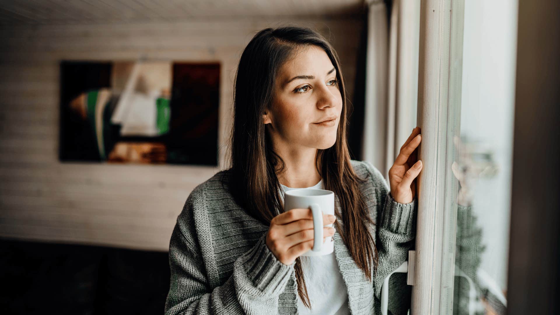 woman drinking tea by a window after speaking blessings into her space