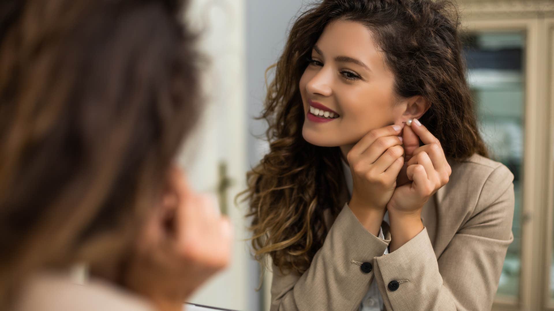 woman putting on earrings in mirror