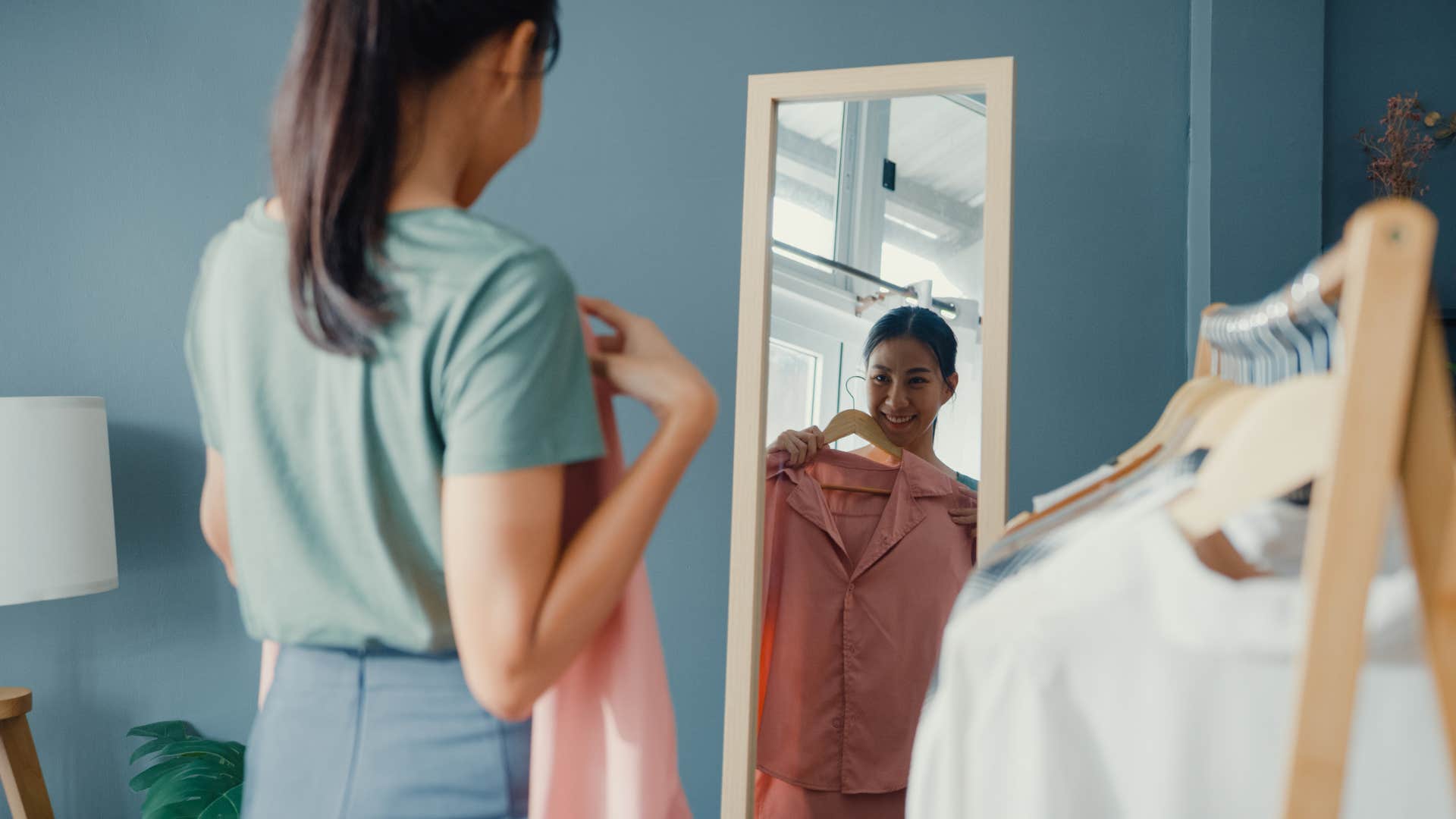 woman holding up shirt to herself in the mirror
