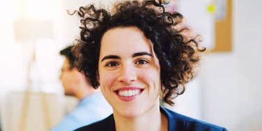 A woman smiles at the camera in a bright indoor setting.