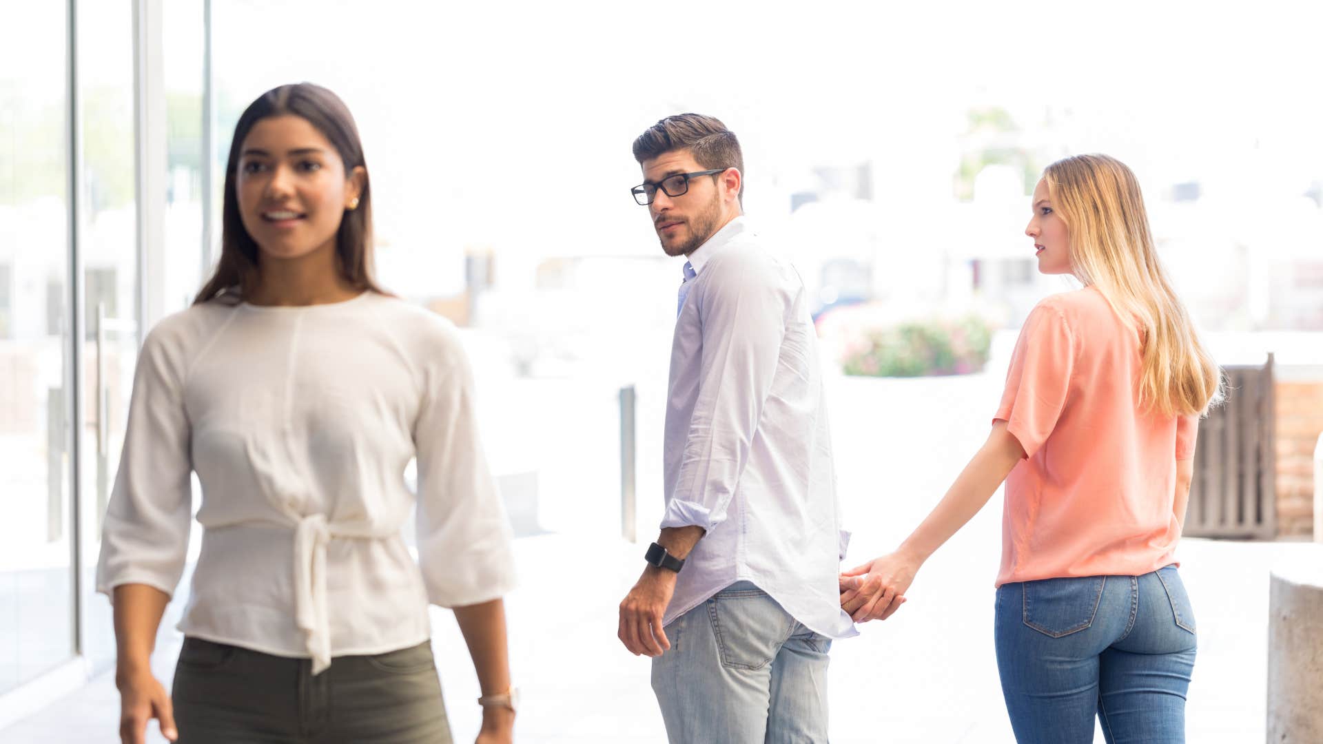 man looking at another woman while holding his partner's hand