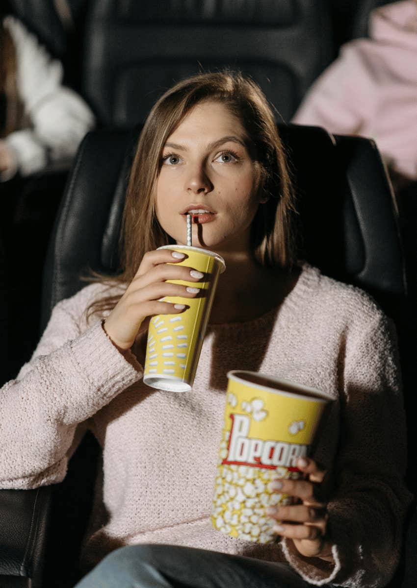 happy woman in a movie theater alone holding drink and popcorn