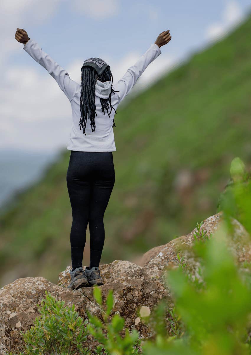 young woman with arms in the air after conquering mountain